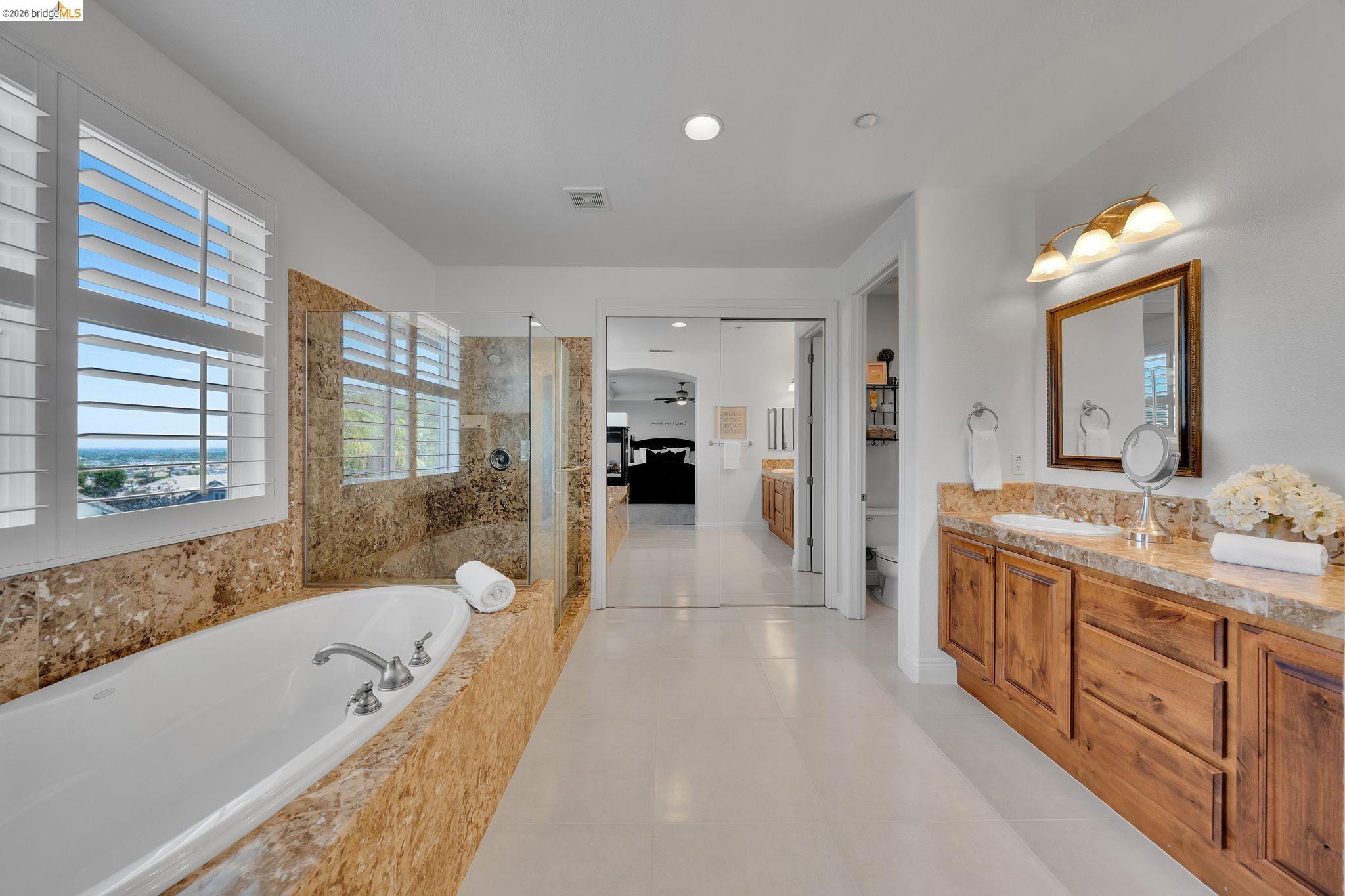 2513 Winged Foot Road Brentwood, CA 94513 - Photo 18 of 45 Bathroom featuring a built-in soaking tub with stone surround, a glass-enclosed shower, dual vanity with undermount sinks and stone countertop, and custom window shutters