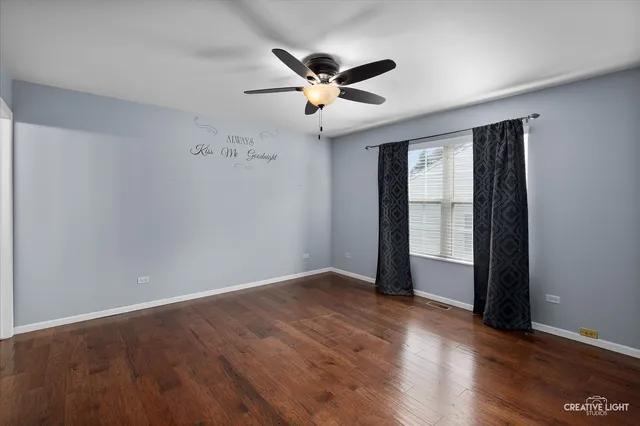 an empty room with wooden floor chandelier fan and windows
