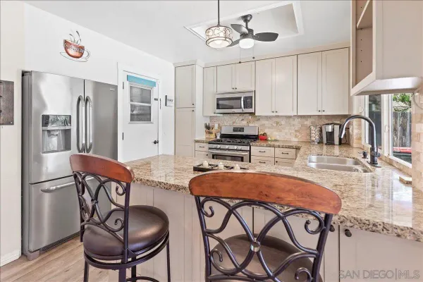 a kitchen with stainless steel appliances granite countertop a dining table chairs refrigerator and sink