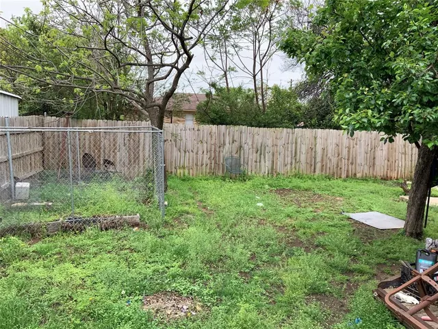 a view of a backyard with large trees and wooden fence