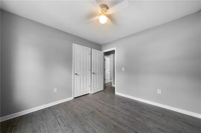 an empty room with wooden floor chandelier fan and windows