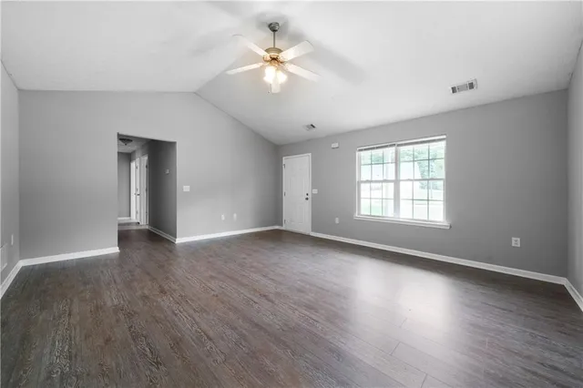 an empty room with wooden floor chandelier fan and windows