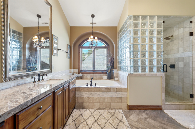 335 Bern Way Midway, UT 84049 - Photo 34 of 88 Spacious bathroom featuring a built-in soaking tub with arched window, a glass block shower enclosure, wood-finish vanity with dual sinks, and light-toned tile flooring