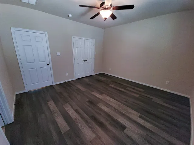 an empty room with wooden floor fan and windows