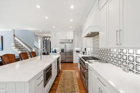 a large white kitchen with stainless steel appliances kitchen island a large counter top and a couch