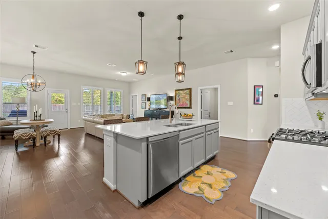 a kitchen with kitchen island a stove a refrigerator a sink a dining table and chairs with wooden floor