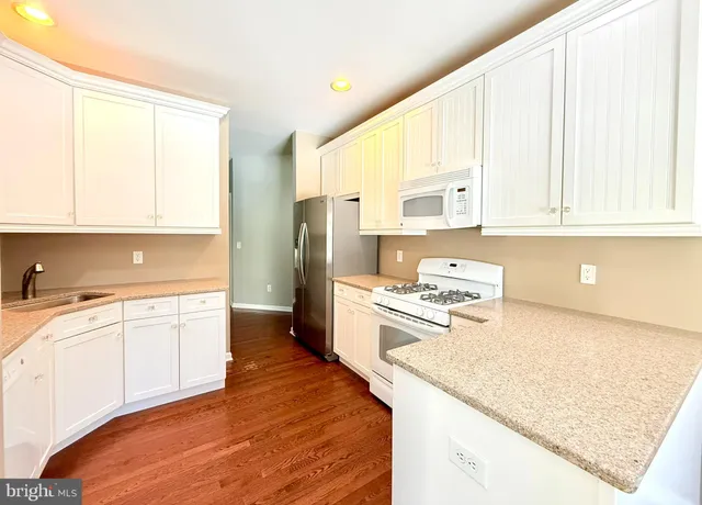 a kitchen with stainless steel appliances granite countertop a stove a sink and white cabinets with wooden floor