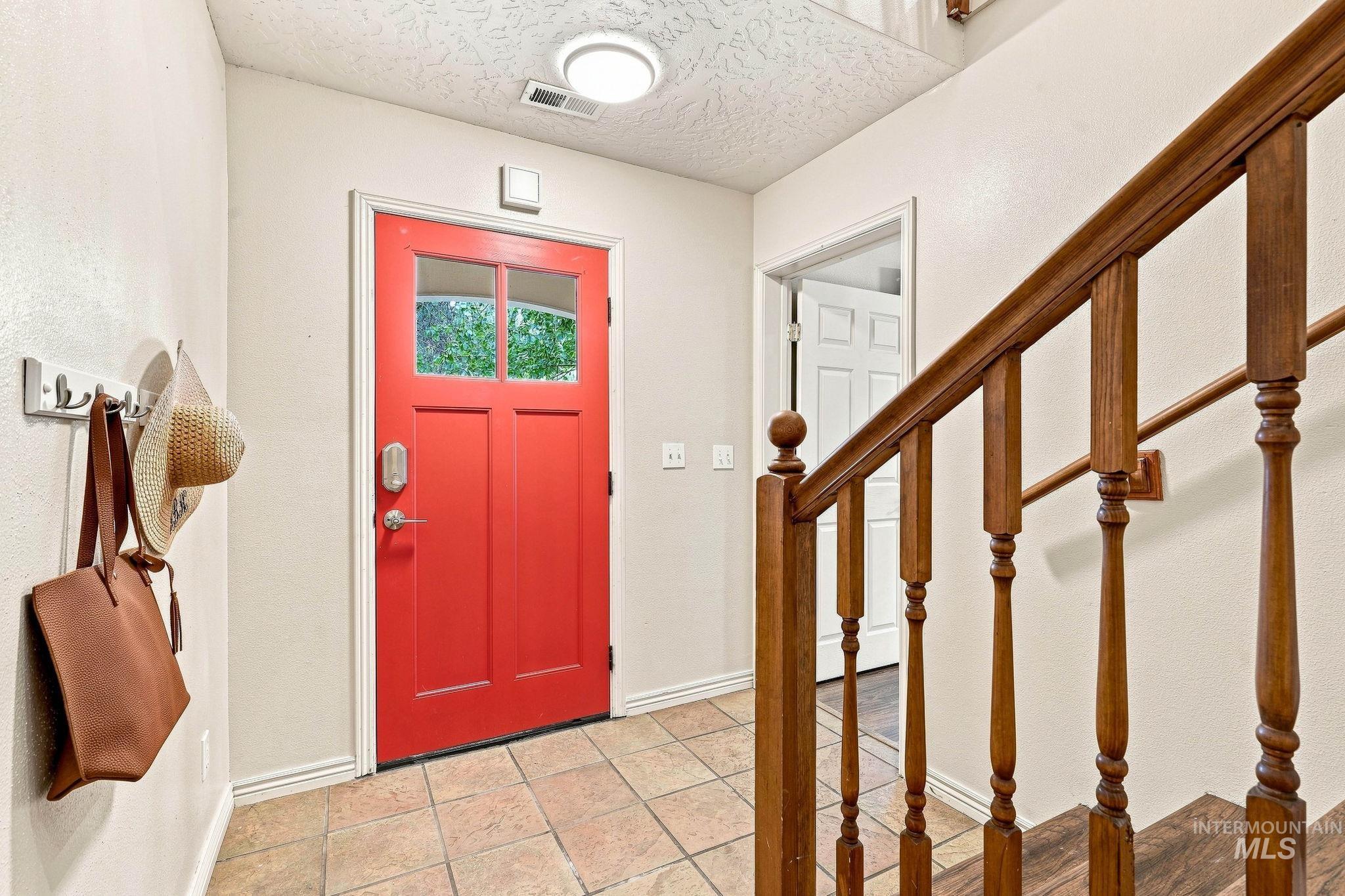 2442 West Hill Road Boise, ID 83702 - Photo 3 of 48 Red paneled entry door with transom windows, tile flooring, and wood stair railing