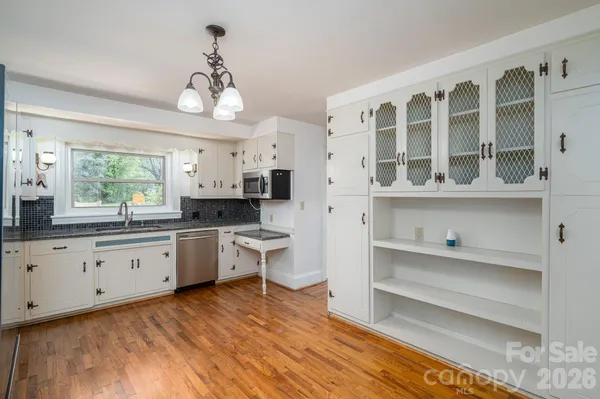 a large white kitchen with granite countertop a stove a sink dishwasher a dining table and chairs with wooden floor