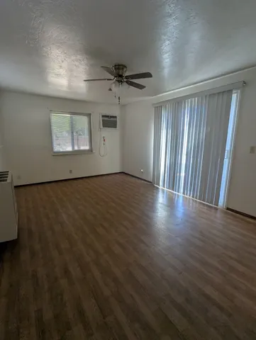 an empty room with wooden floor ceiling fan and windows
