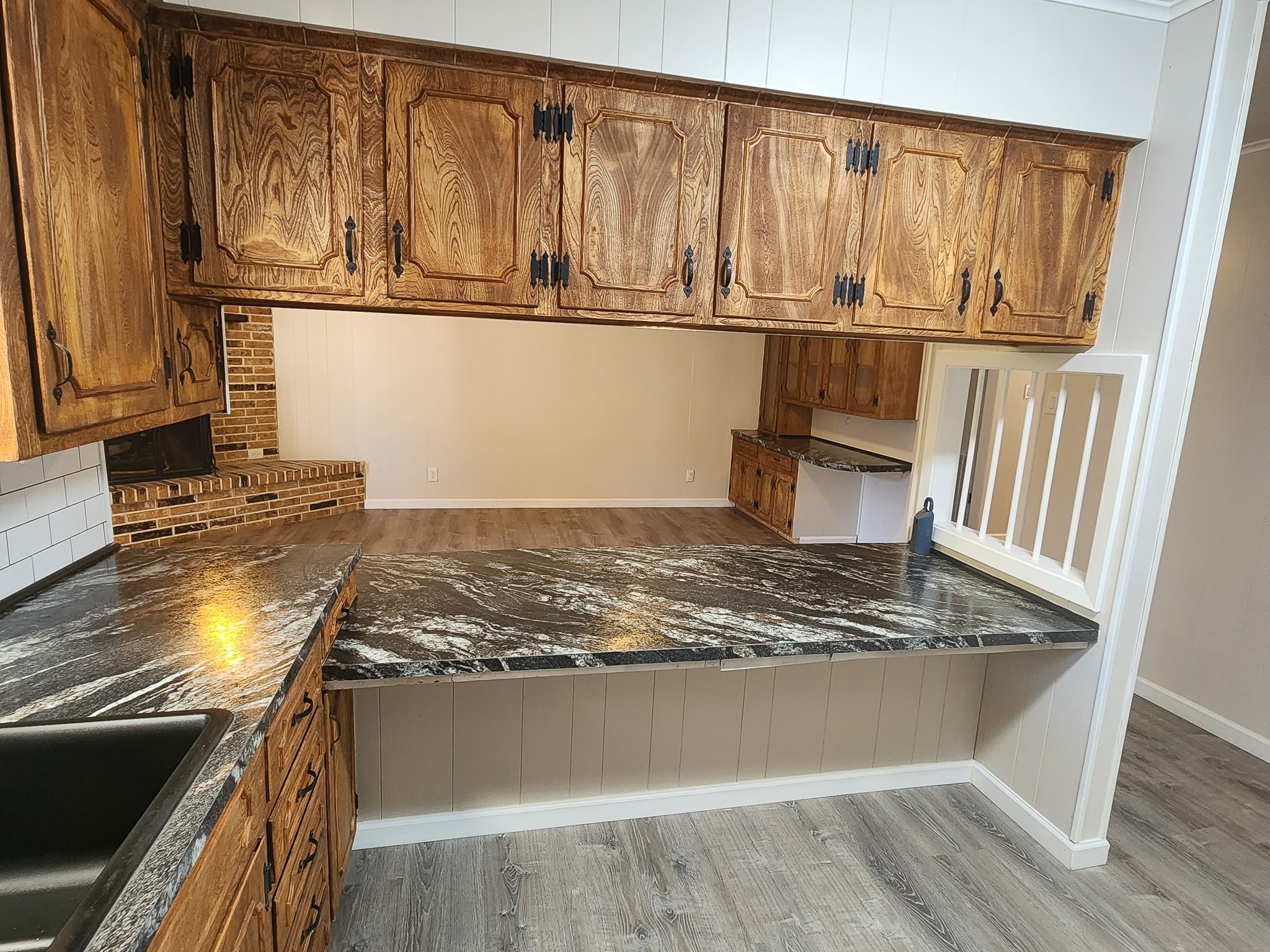201 Verna Street Jasper, TX 75951 - Photo 8 of 24 This kitchen features rustic wooden cabinets, dark stone countertops, and a view into a spacious adjoining room with wood flooring and a brick fireplace. The design offers a blend of classic charm and open concept living.