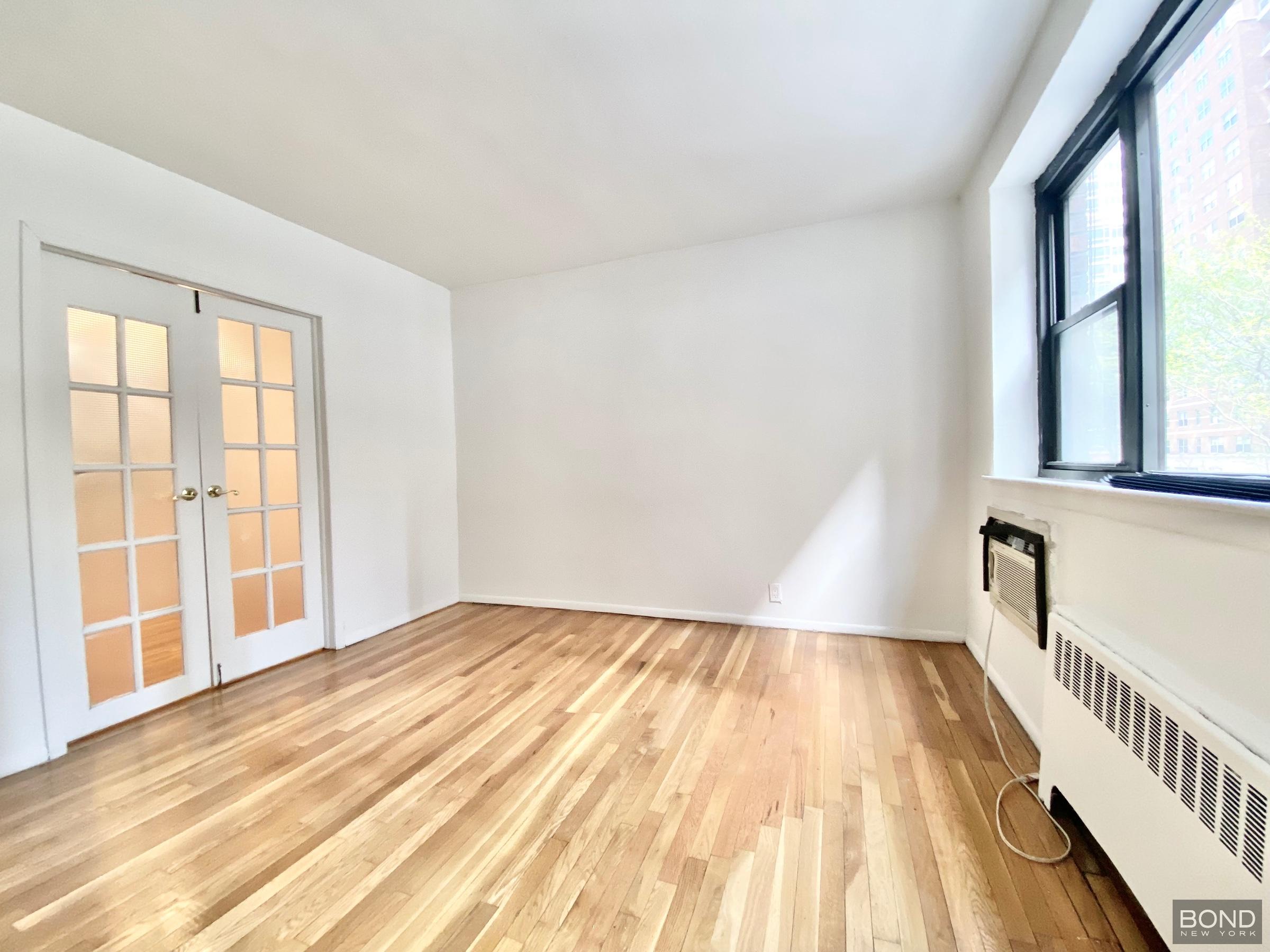 345 East 72nd Street, Unit 2A Manhattan, NY 10021 - Photo 7 of 10 a view of an empty room with wooden floor and a window