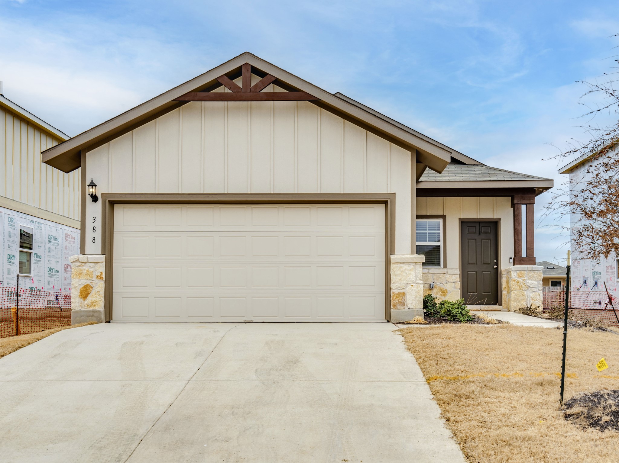 View of front of property with board and batten siding, stone siding, driveway, and a garage
