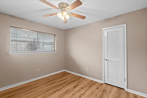 an empty room with wooden floor chandelier fan and windows