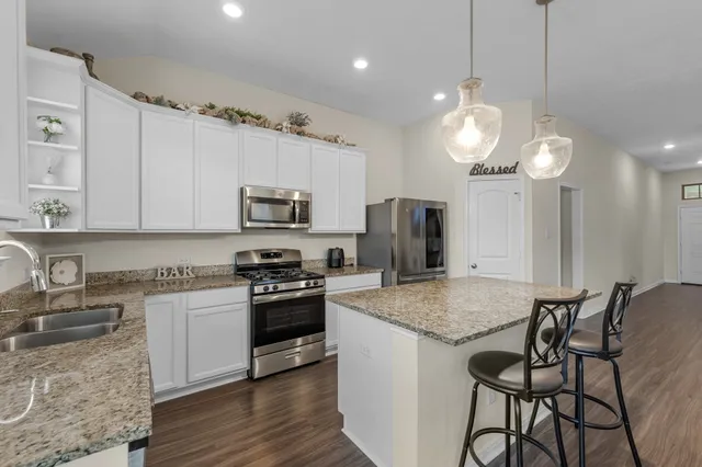 a kitchen with stainless steel appliances granite countertop a stove top oven a refrigerator a sink dishwasher a dining table and chairs with wooden floor