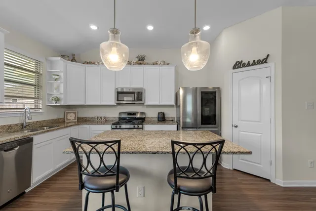 a kitchen with stainless steel appliances granite countertop a stove a sink dishwasher a dining table and chairs with wooden floor