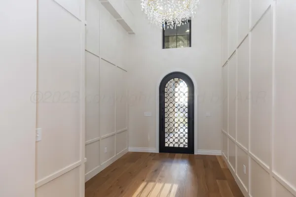a view of an empty room with chandelier and wooden floor