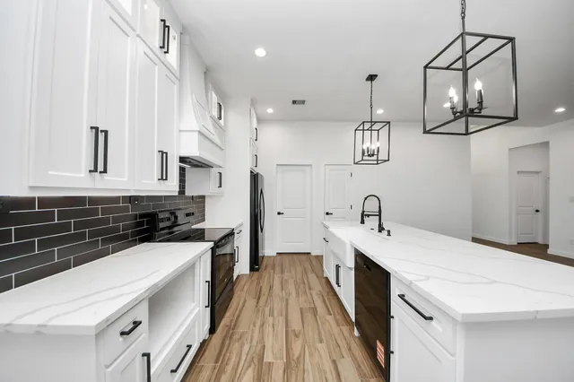 a kitchen with a sink dishwasher a stove and white cabinets with wooden floor
