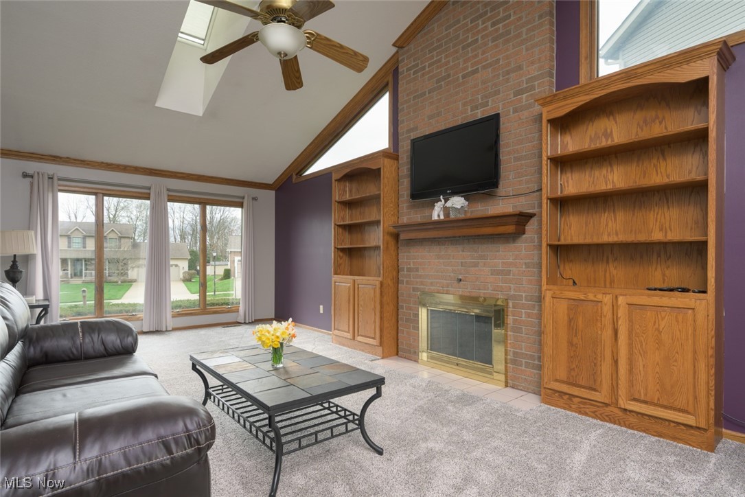819 Bridge Road Akron, OH 44312 - Photo 16 of 33 Living area featuring light carpet, a ceiling fan, a brick fireplace, crown molding, and high vaulted ceiling
