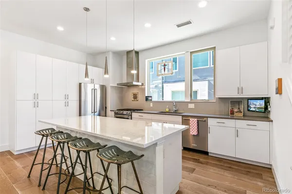 a kitchen with stainless steel appliances granite countertop a stove a sink dishwasher a refrigerator and white cabinets with wooden floor