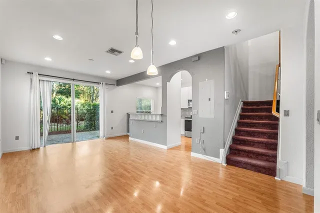 a view of an empty room and kitchen with wooden floor