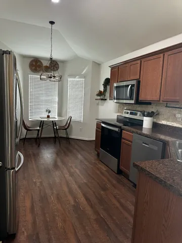 a kitchen with stainless steel appliances granite countertop a refrigerator a stove top oven a sink dishwasher and wooden cabinets with wooden floor