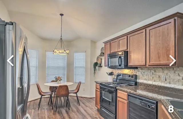 a kitchen with stainless steel appliances granite countertop a stove a refrigerator a sink a dining table and chairs with wooden floor