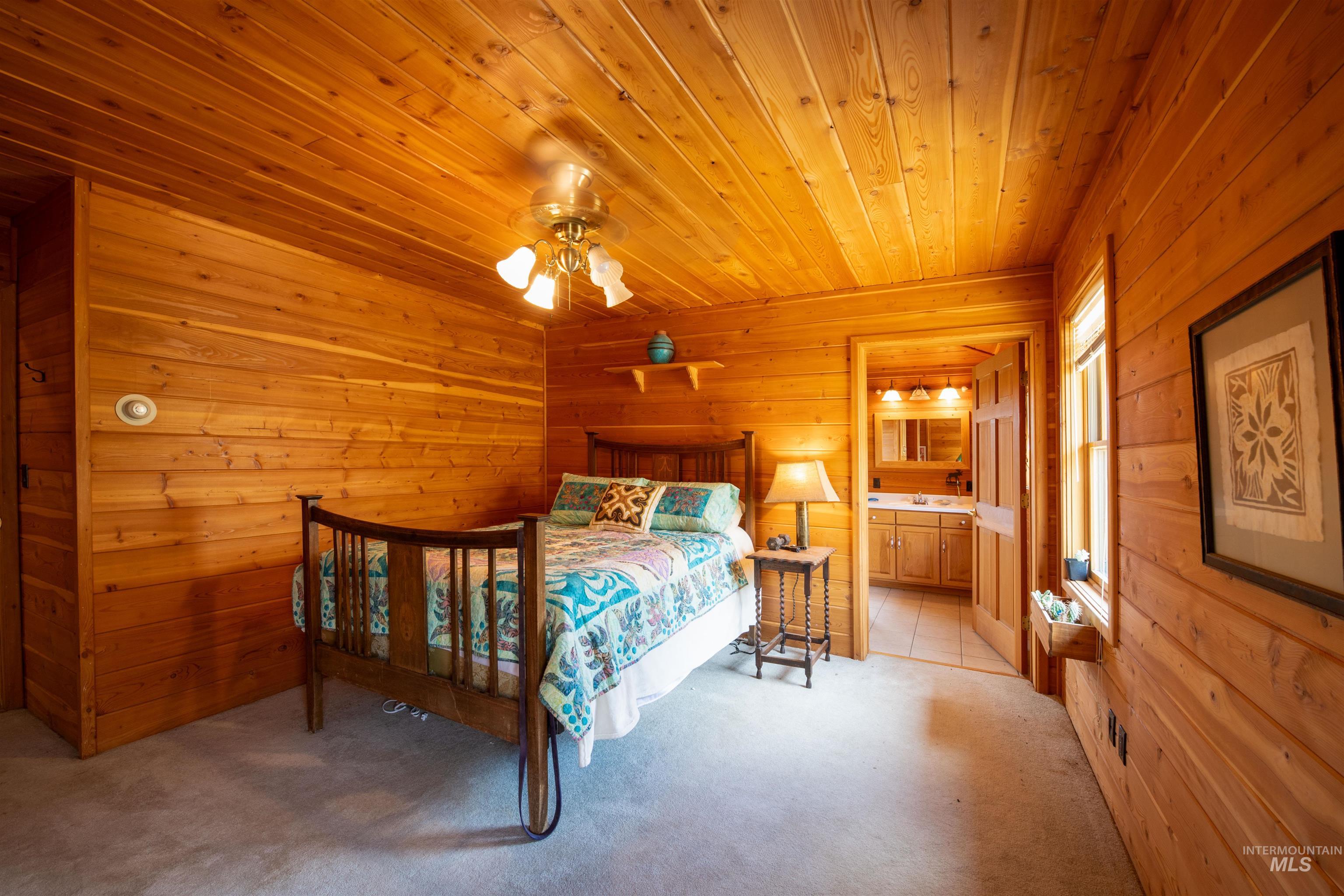 9885 Challis Creek Road Challis, ID 83226 - Photo 20 of 48 Bedroom with wood walls, light colored carpet, wood ceiling, connected bathroom, and a ceiling fan