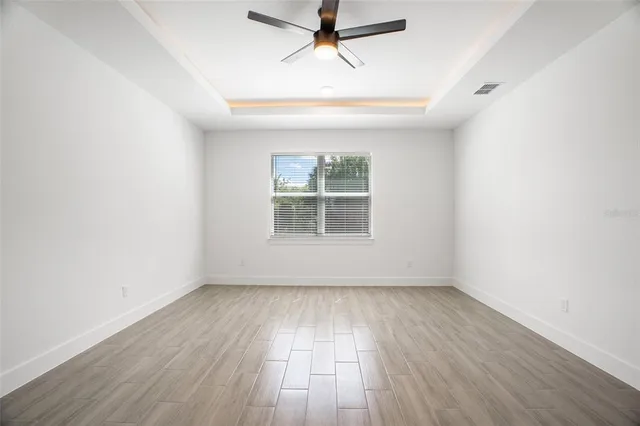 an empty room with wooden floor chandelier fan and windows