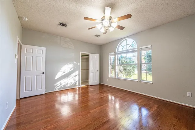 an empty room with wooden floor chandelier fan and windows