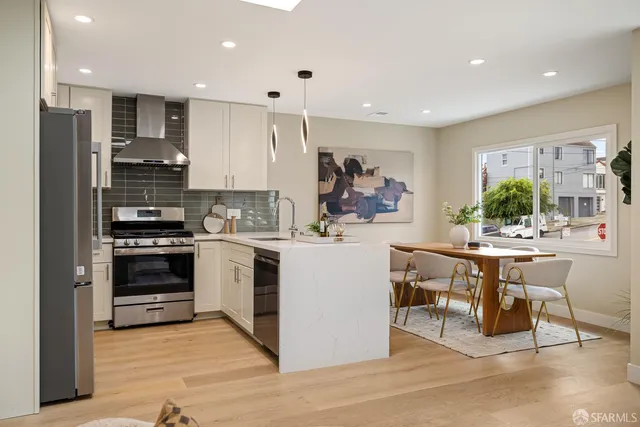 a kitchen with stainless steel appliances kitchen island granite countertop a refrigerator a stove a sink a dining table and chairs with wooden floor