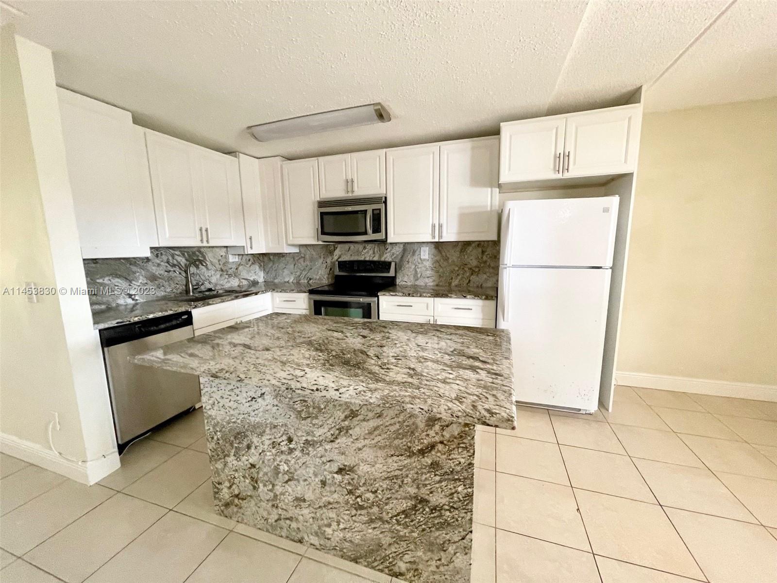 105 Meadows Circle, Unit 105 Boynton Beach, FL 33436 - Photo 5 of 18 a kitchen with granite countertop a refrigerator a stove a microwave a sink and cabinets