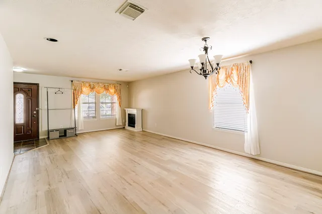 an empty room with wooden floor chandelier and windows
