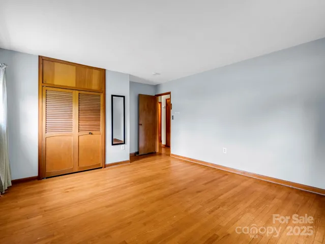 a view of an empty room with wooden floor and kitchen