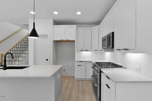 a kitchen that has a sink a microwave oven a stove and white cabinets with wooden floor