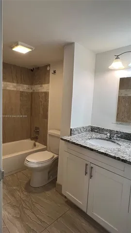 a bathroom with a granite countertop sink a toilet a mirror and bathtub