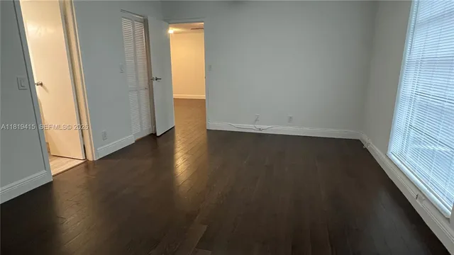 an empty room with wooden floor and windows with curtains