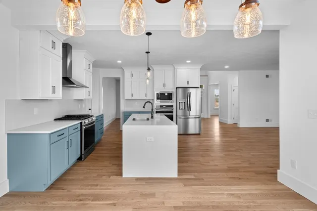 a large white kitchen with kitchen island a stove a sink dishwasher and white cabinets with wooden floor