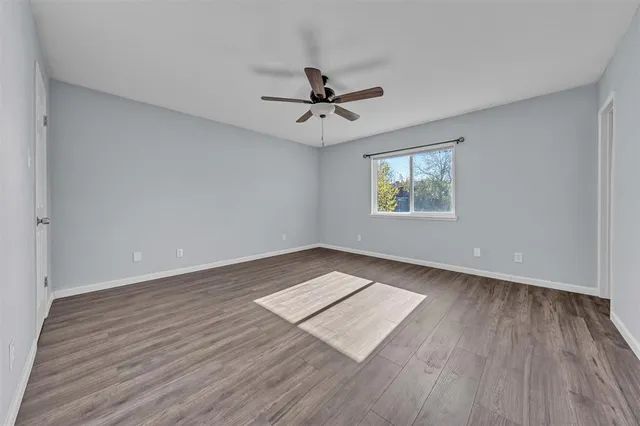 an empty room with wooden floor ceiling fan and windows