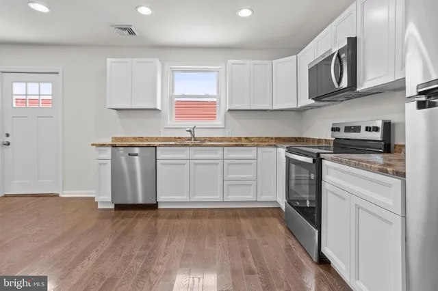 a kitchen with stainless steel appliances granite countertop a stove top oven a sink dishwasher and white cabinets with wooden floor