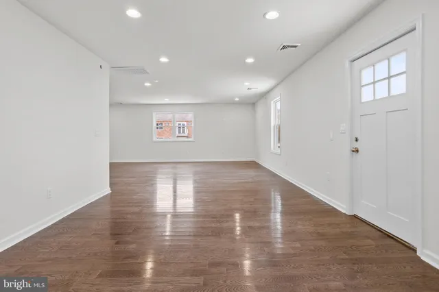 an empty room with wooden floor and windows with curtains