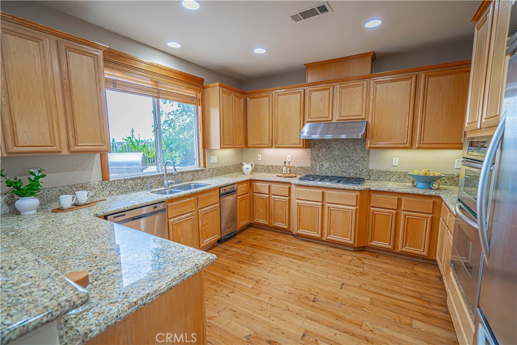 28419 Hidden Hills Drive Saugus, CA 91390 - Photo 16 of 60 a kitchen with granite countertop wooden cabinets a sink a window and stainless steel appliances