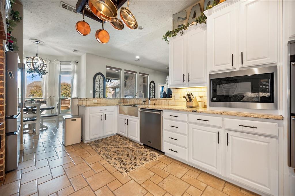 212 Ashmore Place Haslet, TX 76052 - Photo 14 of 39 Kitchen with backsplash, white cabinets, stainless steel appliances, a textured ceiling, and a chandelier