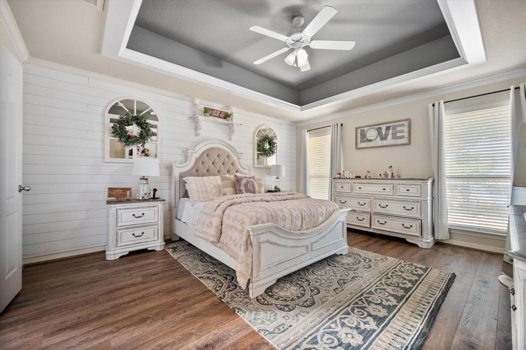 212 Ashmore Place Haslet, TX 76052 - Photo 19 of 39 Bedroom with a tray ceiling, dark wood-type flooring, a ceiling fan, wood walls, and ornamental molding