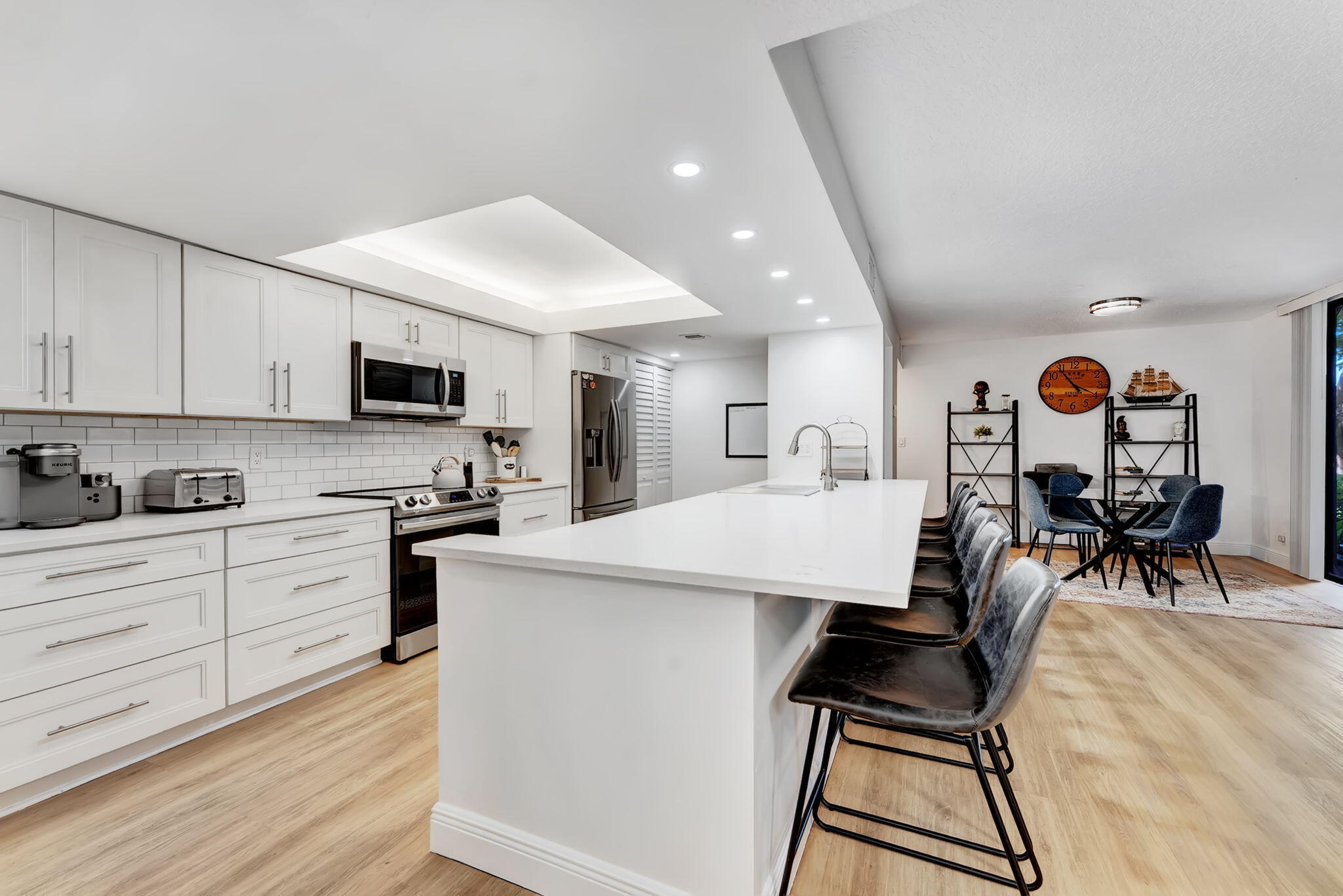 a living room with stainless steel appliances kitchen island granite countertop a sink and white cabinets with wooden floor