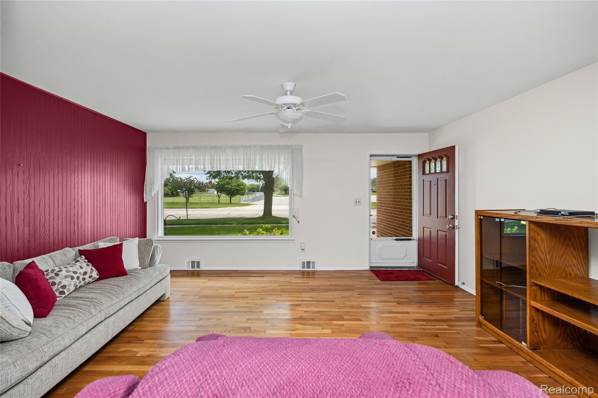 Living area featuring wood-finish flooring, a white ceiling fan, and a front entry door with glass panels