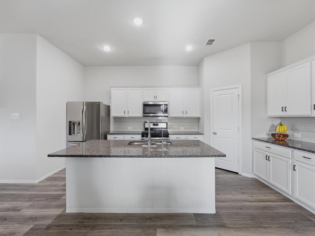 6000 Sutton Fields Trail Aubrey, TX 76227 - Photo 8 of 40 Kitchen with dark stone countertops, stainless steel appliances, decorative backsplash, dark wood-type flooring, and white cabinets