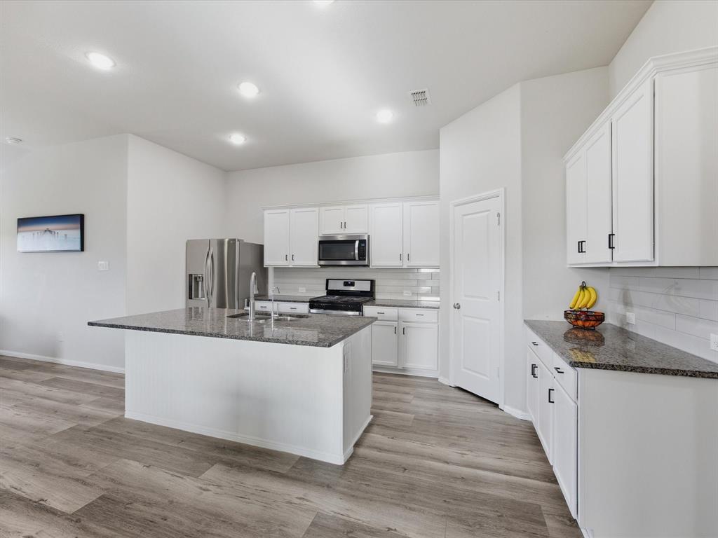 6000 Sutton Fields Trail Aubrey, TX 76227 - Photo 10 of 40 Kitchen with dark stone countertops, white cabinets, stainless steel appliances, backsplash, and a center island with sink