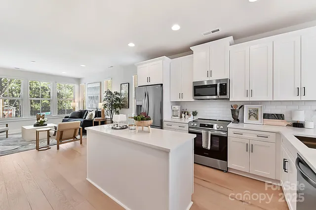 a kitchen with stainless steel appliances granite countertop a stove top oven a sink dishwasher and white cabinets with wooden floor