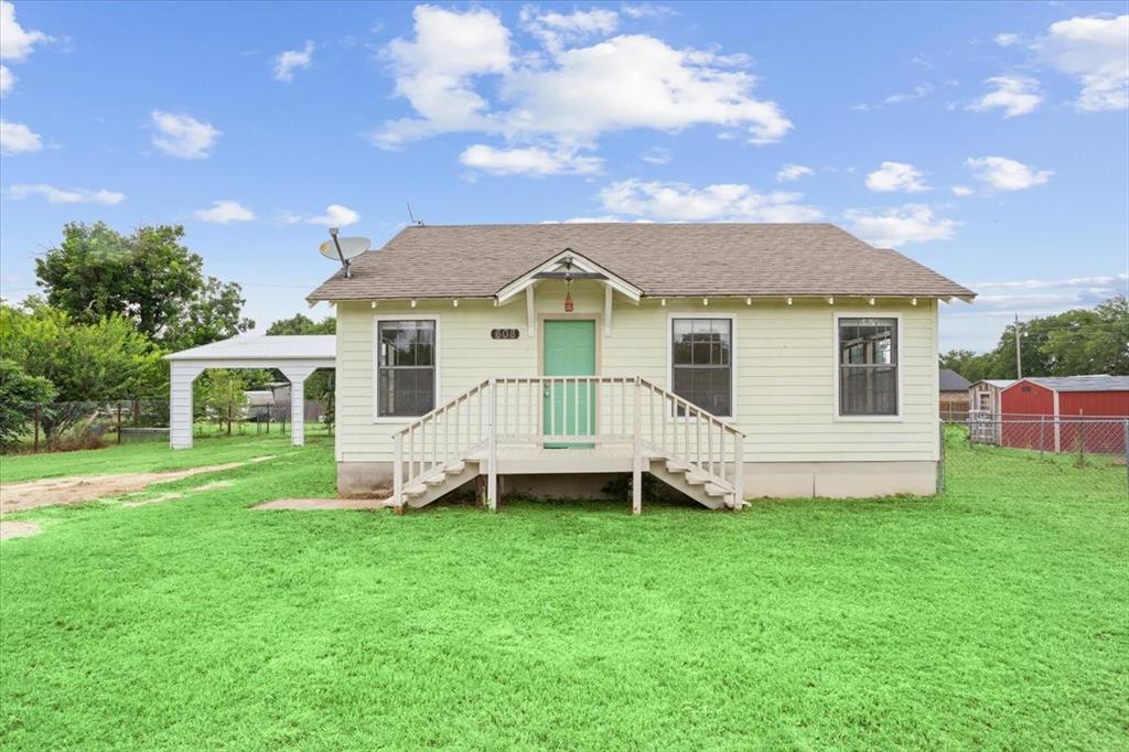 608 9th Street Hico, TX 76457 - Photo 1 of 23 Light yellow siding exterior with a contrasting turquoise front door, featuring a peaked roofline and an elevated front porch with white railings